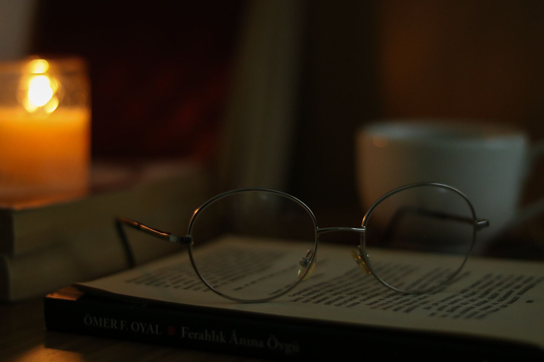 Eyeglasses on an open book with candlelight and a cup of coffee, creating a warm reading atmosphere.