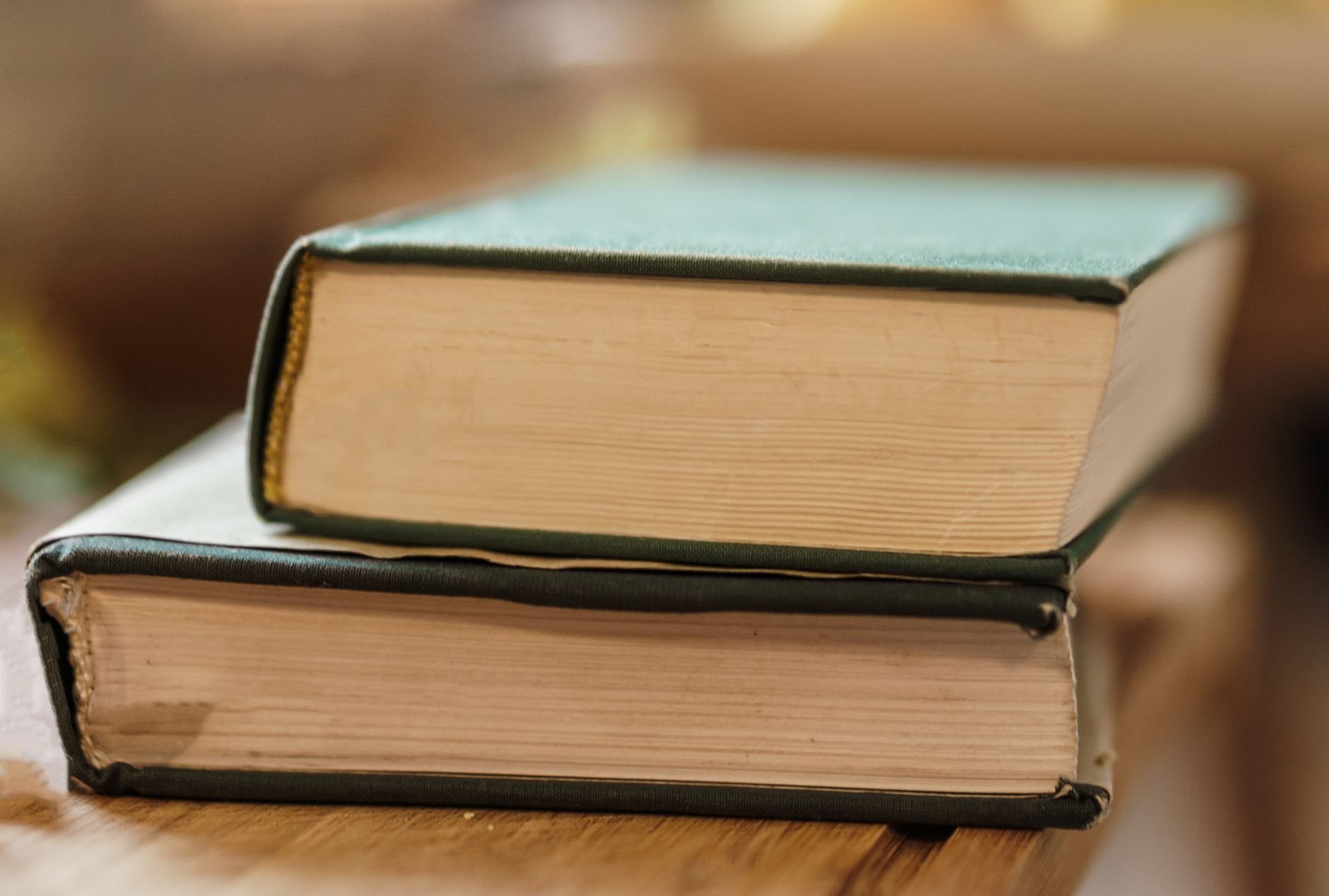 Aged big books with hard covers on wooden desk in shiny light on blurred background